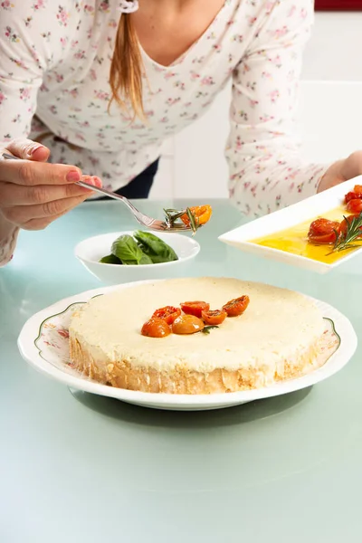 Kızın ellerinin, peynirli keki vişneli domatesle süslediği yakın plan.