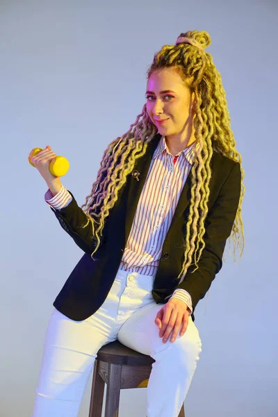 Woman power concept - girl in jeans and jacket with dreadlocks pumps dumbbell