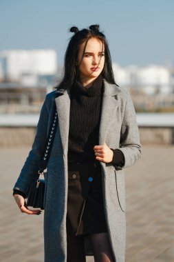 Sokakta ceketli ve kazaklı genç bir kadın var.