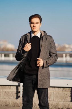Siyah kazaklı, beyaz gömlekli ve siyah kotlu genç adam sokaktaki paltonun zeminini tutuyor.