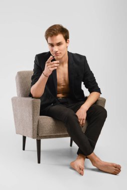 Siyah takım elbiseli genç adam stüdyoda bir koltukta oturuyor ve parmağını ileri uzatıyordu.