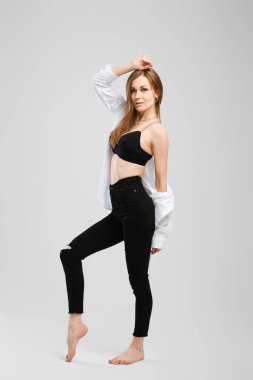 Siyah kot ve gömlekli çıplak ayaklı genç bir kadının stüdyo portresi.