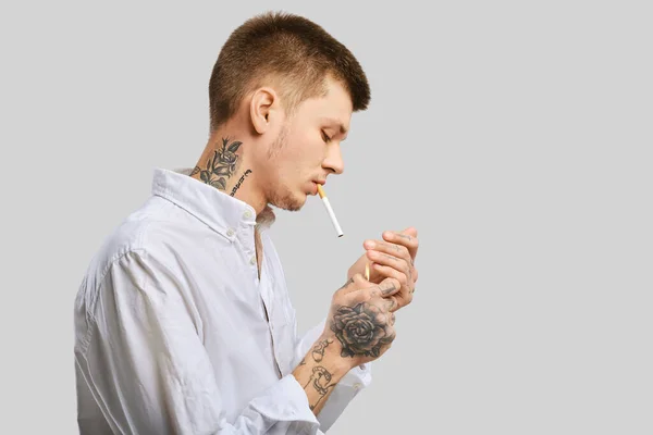 Jonge Getatoeëerde Man Steekt Een Sigaret Studio — Stockfoto