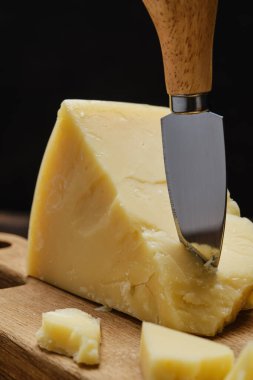 Closeup view of triangular piece of parmesan cheese on wooden cutting board