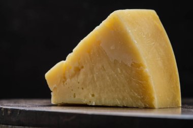 Closeup view of triangular piece of parmesan cheese on wooden cutting board