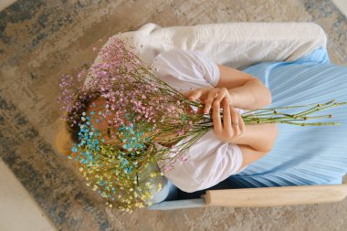 Elinde bahar çiçekleriyle koltukta oturan bir kadına yukarıdan bak.