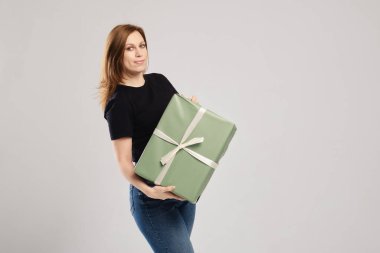 Gri arka planda büyük hediye kutusuyla poz veren genç bir kadın.