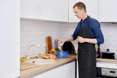 Orta yaşlı bir adam mutfakta omlet yaparken tuz döküyor.
