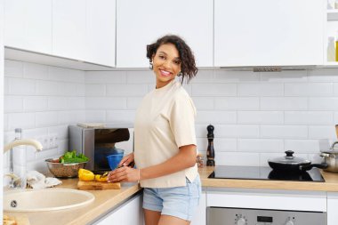 Neşeli Afrikalı Amerikalı kadın sağlıklı sebze salatası pişiriyor, kameraya bakıyor ve gülümsüyor.