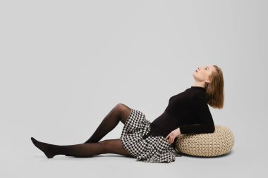 Tam boy stüdyo portresi. Gri arka planda yerde oturan genç bir Wooman resmi.