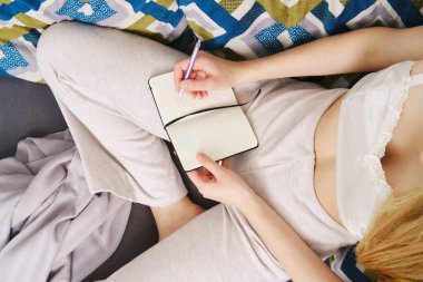 Evdeki kanepede oturan bir deftere not almak (yukarıdan görünüm))