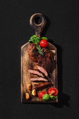 Dökme demir tavada kızartılmış biftek örümceği, ahşap kesme tahtasında domates ve fesleğenle servis ediliyor.