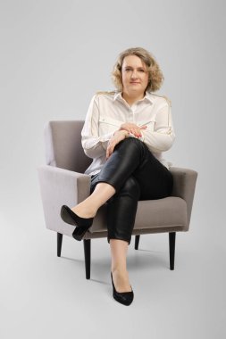 Beyaz gömlekli, çapraz kollu, kendinden emin yaşlı bir kadının tüm vücut portresi.