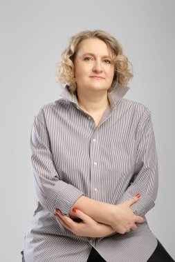 Kollarını kavuşturmuş gri gömlekli yaşlı bir kadının stüdyo portresi.