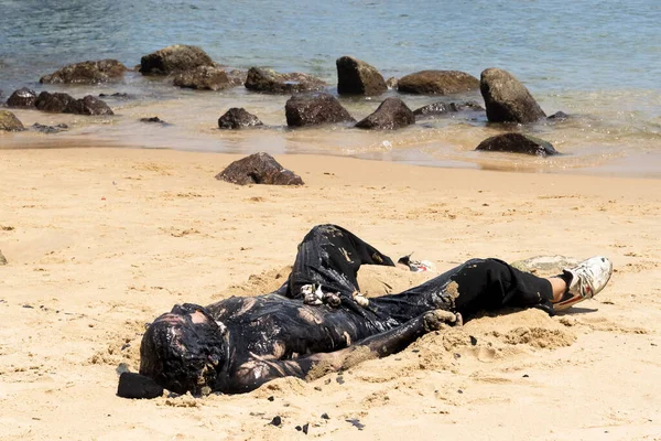 Man covered in oil on the beach at Porto da Barra in Salvador, Bahia, in protest of oil spilled by a ship on the beaches of Brazil.