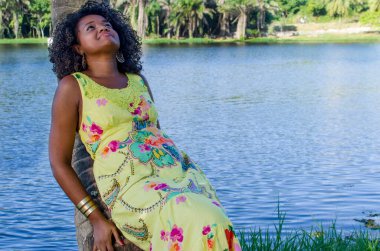 Siyah kadın fotoğraf için poz veriyor. Gülümsüyor ve kameraya bakıyor. Arka plandaki ağaçlar, nehir ve bitkiler. Salvador, Bahia, Brezilya.