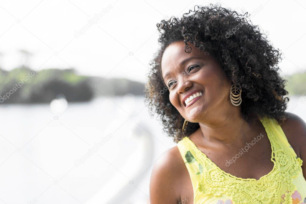 Black woman posing for photo. She wears yellow, smiles and looks at the camera. Salvador, Bahia, Brazil.