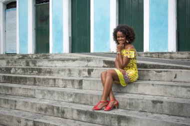 Sarı elbiseli, gülümseyen ve kameraya poz veren bir manken. Arka planda, antik mimarisi ile Pelourinho 'nun tarihi merkezi. Salvador Bahia Brezilya.