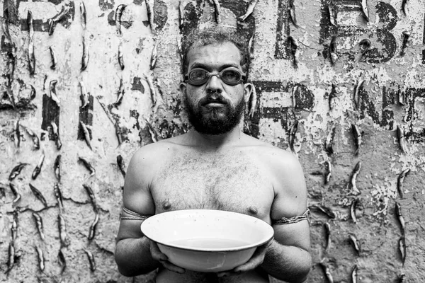 Man performs protest performance at the Sao Joaquim fair in Salvador. He is shirtless, holds a white basin of water, and wears diving goggles. Salvador Bahia Brazil.