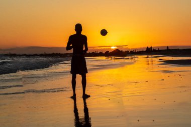 Genç model kumsalda güzel sarı günbatımında kum futbolu oynuyor. Salvador Bahia Brezilya.