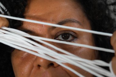 Açık gri arka planda elinde askılı iple renkli elbiseler giyen bir kadının yakın çekimi. Salvador, Bahia, Brezilya.