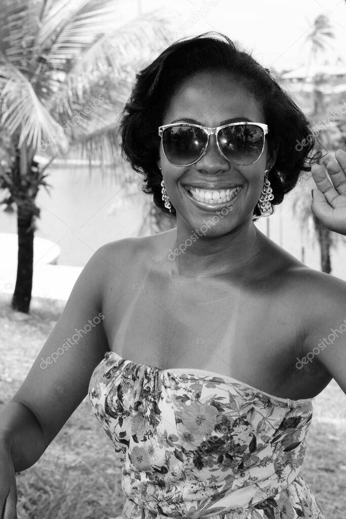Black woman posing for photo. She is smiling and looking at the camera. In the background, nature in trees and plants. Salvador, Bahia, Brazil