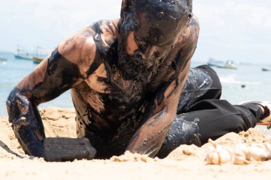 Adam Salvador 'daki Porto da Barra plajında Sarımsak ve Yağ' ın tiyatro performansını sergiliyor. Tamamen siyah boya, sarımsak ve yağla kaplı. Salvador Bahia Brezilya.