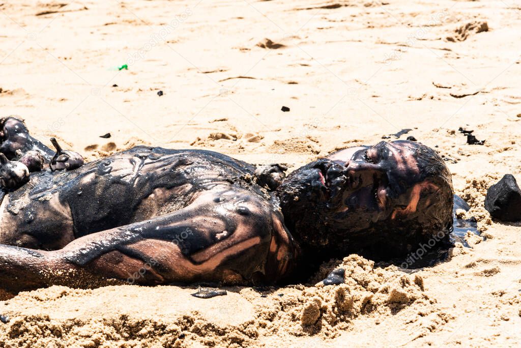 Man performs theatrical performance of Garlic and Oil on the Porto da Barra beach in Salvador. It is completely covered in black paint, garlic and oil. Salvador Bahia Brazil.