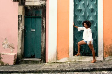 Sarı elbiseli, gülümseyen ve kameraya poz veren bir manken. Arka planda, antik mimarisi ile Pelourinho 'nun tarihi merkezi. Salvador Bahia Brezilya.