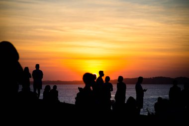Salvador, Bahia, Brezilya - 12 Haziran 2021: Salvador, Bahia 'da Farol da Barra' nın muhteşem renkli günbatımının tadını çıkaran insanların silueti.
