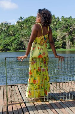 Portrait of a beautiful black woman standing on the edge of a pier against the background of a lake and trees. Salvador, Bahia, Brazil.