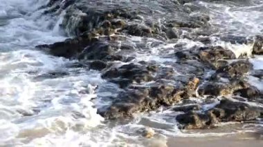 Kumsal dalgaları kum ve kayalara çarpıyor..