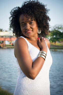 Beyaz elbiseli güzel bir manken gülümsüyor ve kameraya bakıyor. Arka planda, ağaçlar, bitkiler, çiçekler ve manzaradaki nehir. Salvador Bahia Brezilya.