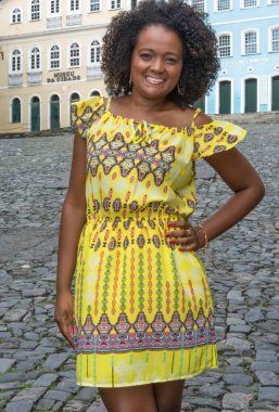 Sarı elbiseli, gülümseyen ve kameraya poz veren bir manken. Arka planda, antik mimarisi ile Pelourinho 'nun tarihi merkezi. Salvador Bahia Brezilya.