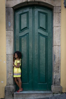 Sarı elbiseli, gülümseyen ve kameraya poz veren bir manken. Arka planda, antik mimarisi ile Pelourinho 'nun tarihi merkezi. Salvador Bahia Brezilya.