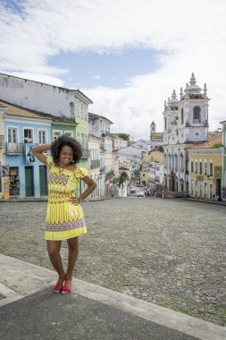 Sarı elbiseli, gülümseyen ve kameraya poz veren bir manken. Arka planda, antik mimarisi ile Pelourinho 'nun tarihi merkezi. Salvador Bahia Brezilya.