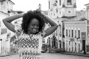 Sarı elbiseli, gülümseyen ve kameraya poz veren bir manken. Arka planda, antik mimarisi ile Pelourinho 'nun tarihi merkezi. Salvador Bahia Brezilya.