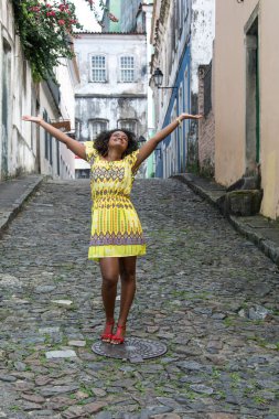 Sarı elbiseli, gülümseyen ve kameraya poz veren bir manken. Arka planda, antik mimarisi ile Pelourinho 'nun tarihi merkezi. Salvador Bahia Brezilya.