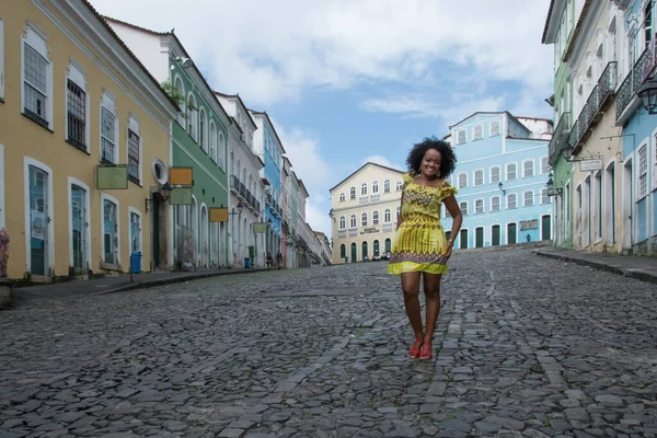 Sarı elbiseli, gülümseyen ve kameraya poz veren bir manken. Arka planda, antik mimarisi ile Pelourinho 'nun tarihi merkezi. Salvador Bahia Brezilya.