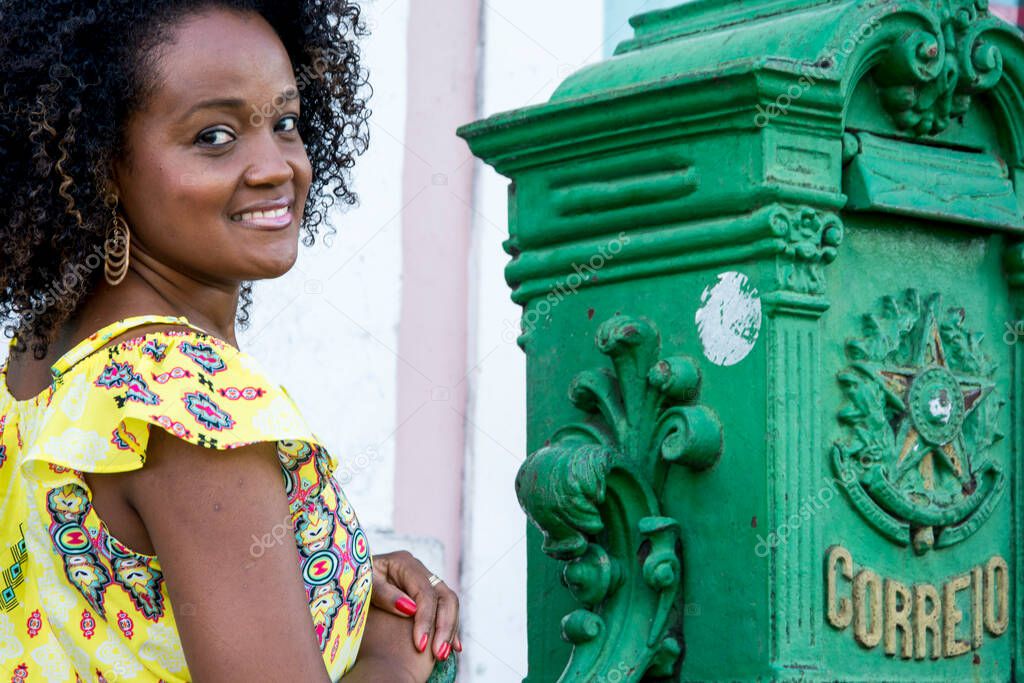 Model in a yellow dress smiling, looking and posing at the camera. In the background, the historical center of Pelourinho with its ancient architecture. Concept of joy, belonging and maturity. Salvador Bahia Brazil.