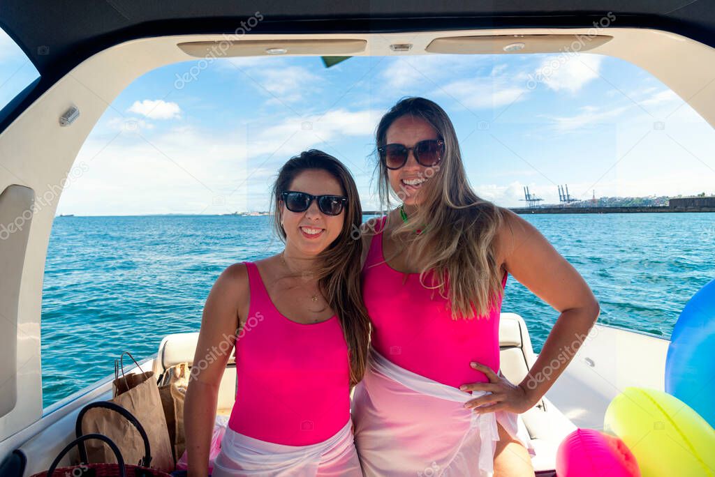 Female friends on top of a boat against the sea in the background. Salvador, Bahia, Brazil.