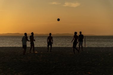 Salvador, Bahia, Brezilya - 23 Aralık 2020: Gençler gün batımında Brezilya 'nın Bahia kentindeki Ribeira plajında plaj futbolu oynuyorlar.