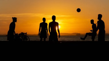 Salvador, Bahia, Brezilya - 23 Aralık 2020: Gençler gün batımında Brezilya 'nın Bahia kentindeki Ribeira plajında plaj futbolu oynuyorlar.