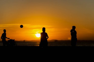 Salvador, Bahia, Brezilya - 23 Aralık 2020: Gençler gün batımında Brezilya 'nın Bahia kentindeki Ribeira plajında plaj futbolu oynuyorlar.