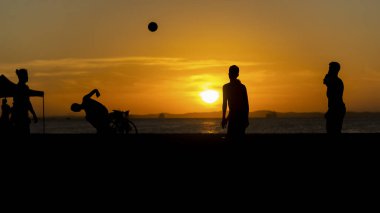 Salvador, Bahia, Brezilya - 23 Aralık 2020: Gençler gün batımında Brezilya 'nın Bahia kentindeki Ribeira plajında plaj futbolu oynuyorlar.