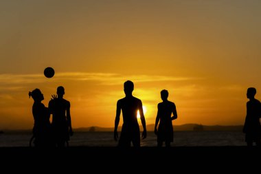 Salvador, Bahia, Brezilya - 23 Aralık 2020: Gençler gün batımında Brezilya 'nın Bahia kentindeki Ribeira plajında plaj futbolu oynuyorlar.