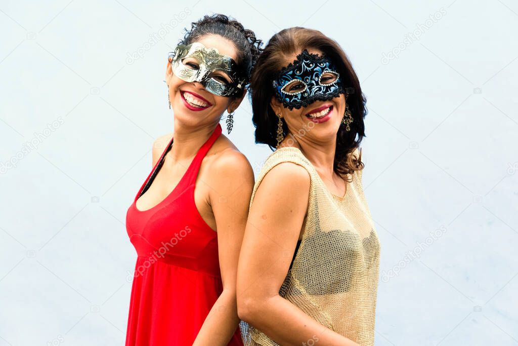 Portrait of two women wearing Venice Carnival mask against light background. Salvador, Bahia, Brazil.