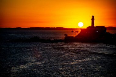 Salvador, Bahia, Brezilya - 19 Eylül 2021: Brezilya 'nın Bahia eyaletindeki Barra plajında güzel ve dramatik bir turuncu gün batımına karşı bir deniz fenerinin silueti.