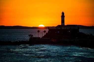 Salvador, Bahia, Brezilya - 19 Eylül 2021: Brezilya 'nın Bahia eyaletindeki Barra plajında güzel ve dramatik bir turuncu gün batımına karşı bir deniz fenerinin silueti.