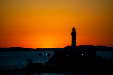 Salvador, Bahia, Brezilya - 19 Eylül 2021: Brezilya 'nın Bahia eyaletindeki Barra plajında güzel ve dramatik bir turuncu gün batımına karşı bir deniz fenerinin silueti.